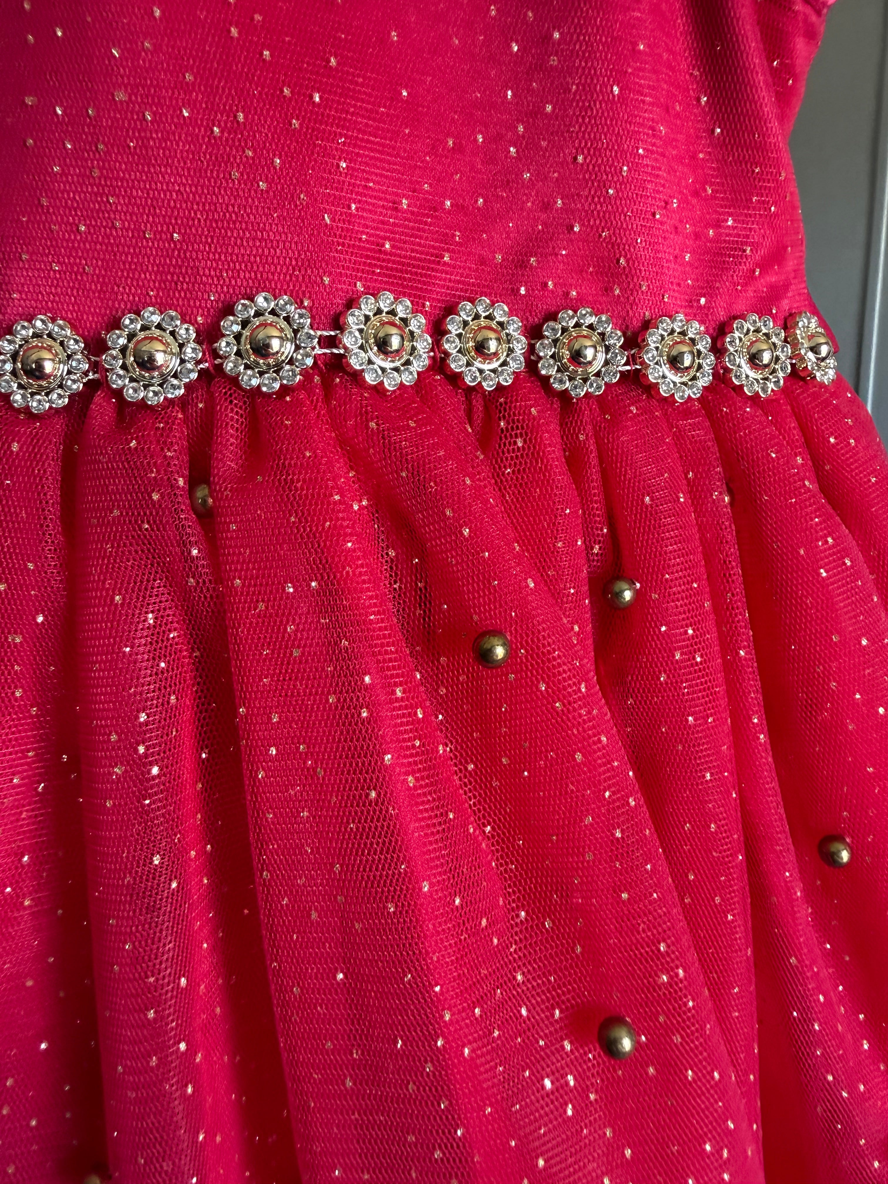 Close-up of a bright red sheer mesh fabric with small metallic gold dots, a decorative waistband of jeweled floral embellishments, and scattered gold metallic bead accents.